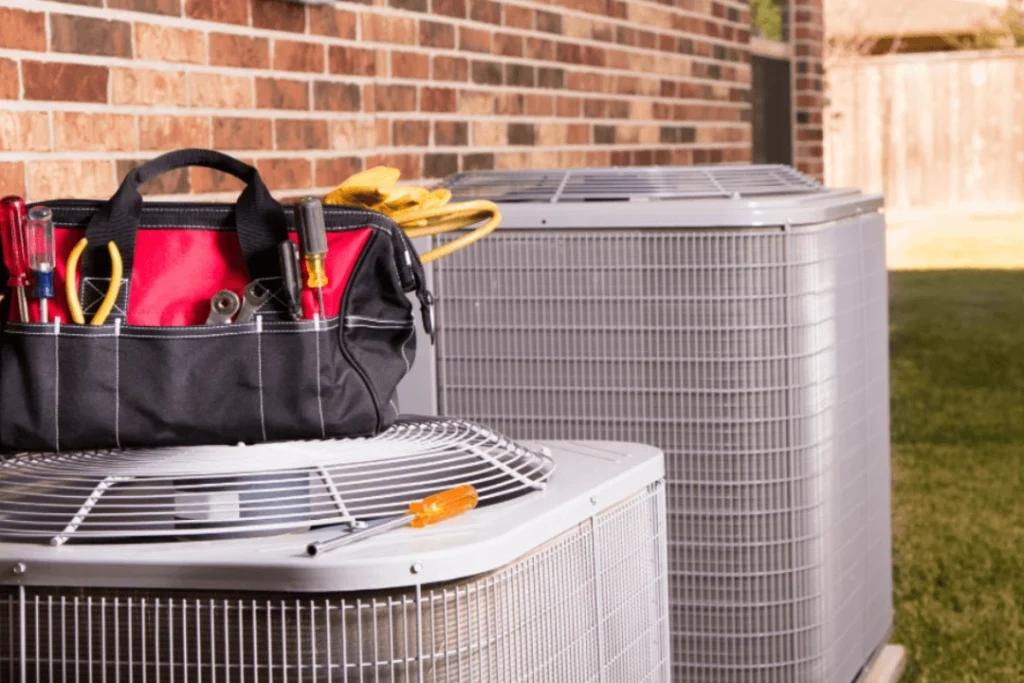 A tool bag filled with various hand tools is placed on top of an outdoor air conditioning unit.