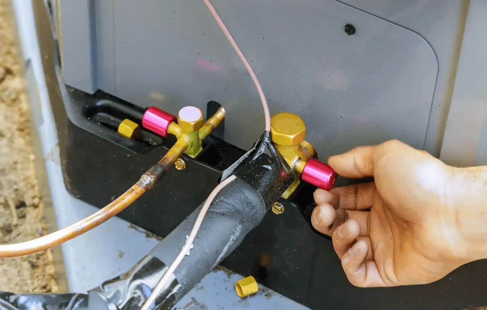 Close-up of a person's hand holding a valve on a hose attached to an air conditioner.